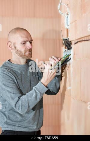 Électricien au travail l'installation de sockets de maison inachevée construite de briques de bloc d'argile. Le travailleur câbles à l'intérieur de maison en construction. Banque D'Images