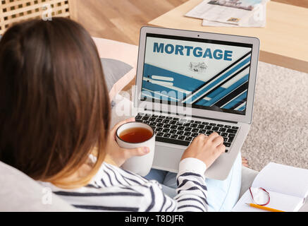 Femme à boire le thé pendant l'utilisation d'ordinateur portable pour payer en ligne à la maison de prêt hypothécaire Banque D'Images