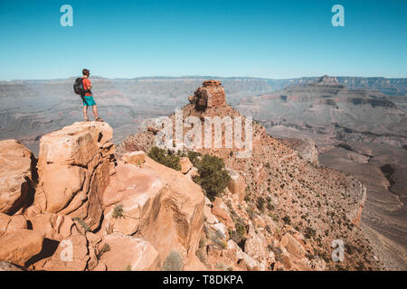 Un jeune male hiker est debout sur un rocher profitant de la magnifique vue sur la célèbre Grand Canyon avec le fleuve Colorado qui coule sur une belle journée ensoleillée Banque D'Images