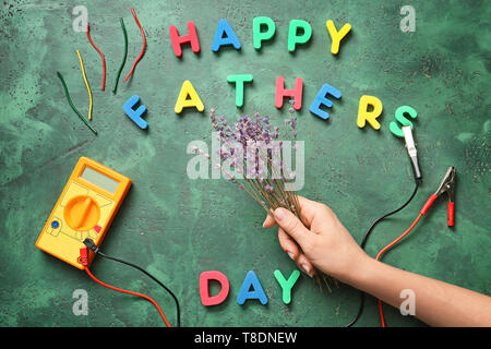 Main tenant plus de fleurs femelles avec un multimètre de table et lettres formant phrase 'Happy Father's Day' Banque D'Images