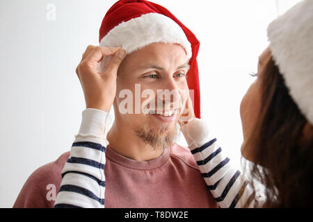 Jeune femme en aidant son petit ami à mettre sur Santa hat against white background Banque D'Images