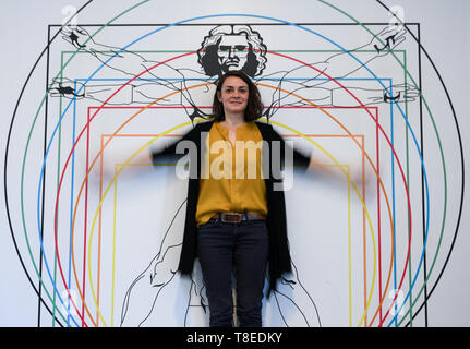 Hessen, Allemagne. 13 mai 2019, 13 mai 2019, Hessen, Gießen : Lisa Peter, employé du musée interactif 'Mathematikum', se trouve dans l'exposition permanente en face de l'image de l'homme Leonardo, un "proportion selon l'étude.' Vitruv Les visiteurs peuvent aller dans une exposition à toucher sur les traces de Léonard de Vinci. À environ 20 stations et des expositions, ils peuvent essayer de faire savoir si les machines dessiné par l'artiste de la Renaissance fonctionnent vraiment et de ce qui se cache derrière ses idées. Le spectacle 'Leonardo, dans le Mathematikum" se déroule du 18 mai 2019 au 29 mars 2020. Dpa : Crédit photo alliance/Alamy Live News Banque D'Images