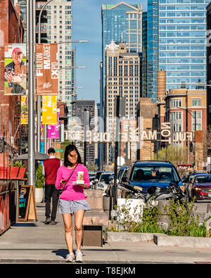 Fulton Market, Chicago-May 4, 2019 : une femme marche et holding coffee sur Fulton Market Street. Les immeubles de grande hauteur dans la distance. Main street dans le quartier chic de Banque D'Images