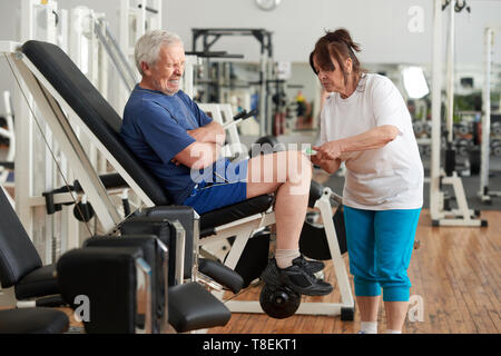 Hauts homme souffrant d'une douleur au genou après wokout. Femme âgée l'application de pommade crème sur mans blessé à la jambe de sport. Les droits de l'expression de la douleur. Banque D'Images