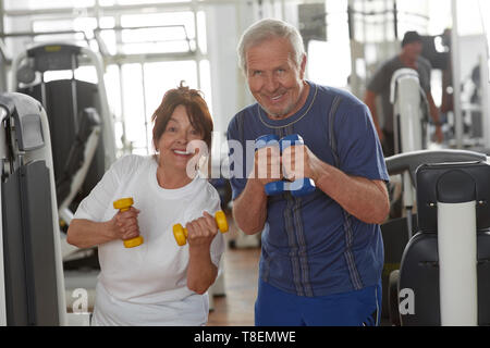 Beau couple de personnes âgées dans une salle de sport. Heureux couple holding dumbbells fitness and smiling at camera au club de remise en forme. Condition physique pour les adultes plus âgés. Banque D'Images