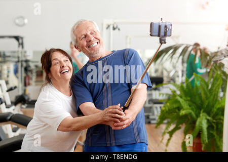 Smiling couple âgé en tenant à selfies sport. Beaux cadres supérieurs se reposant dans une salle de sport en tenant avec selfies monopod. Les gens, le sport, la technologie moderne et l Banque D'Images