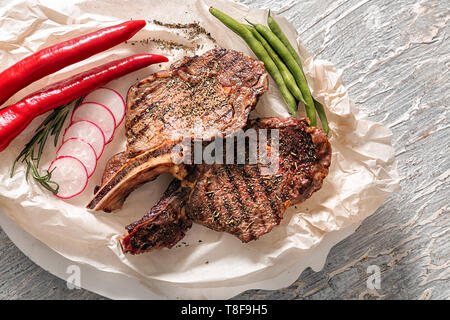 Parchemin avec de délicieux steaks grillés et légumes sur table en bois clair Banque D'Images