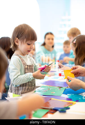 Groupe d'enfants avec l'enseignant du projet faire en maternelle. Enfant fille avec des ciseaux dans les mains dans la salle de classe. Les enfants jouent en équipe. Banque D'Images