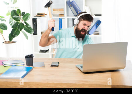 Homme barbu bureau écouteurs swing marteau sur ordinateur. Connexion internet lente. Logiciel obsolète. Décalage de l'ordinateur. Pour des raisons du retard de l'ordinateur. Comment fixer la traîne lente du système. La routine du bureau. Banque D'Images