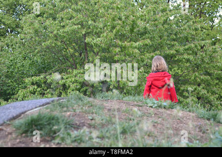 Little girl dans un manteau rad marche dans la nature tout seul, par ses propres, vu de derrière