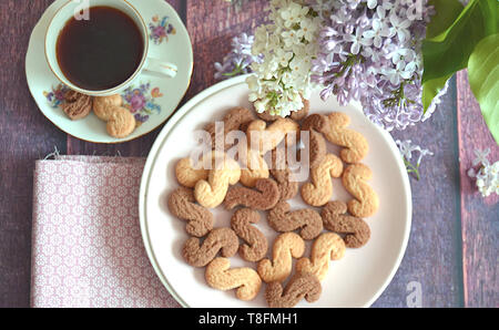 Tchèque traditionnel de la cannelle & cacao biscuits Esicka sur une plaque sur une table en bois avec un vieux-fashionned tasse de thé et de fleurs lilas. Banque D'Images