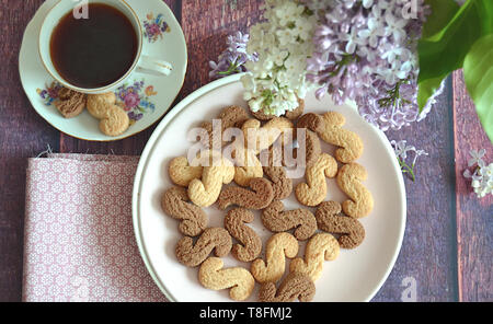 Tchèque traditionnel de la cannelle & cacao biscuits Esicka sur une plaque sur une table en bois avec un vieux-fashionned tasse de thé et de fleurs lilas. Banque D'Images