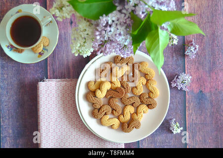 Tchèque traditionnel de la cannelle & cacao biscuits Esicka sur une plaque sur une table en bois avec un vieux-fashionned tasse de thé et de fleurs lilas. Banque D'Images