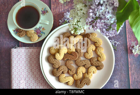 Tchèque traditionnel de la cannelle & cacao biscuits Esicka sur une plaque sur une table en bois avec un vieux-fashionned tasse de thé et de fleurs lilas. Banque D'Images