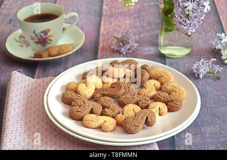 Tchèque traditionnel de la cannelle & cacao biscuits Esicka sur une plaque sur une table en bois avec un vieux-fashionned tasse de thé et de fleurs lilas. Banque D'Images