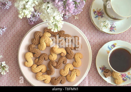 Tchèque traditionnel de la cannelle & cacao biscuits Esicka sur une plaque sur une table en bois avec un vieux-fashionned tasse de thé et de fleurs lilas. Banque D'Images