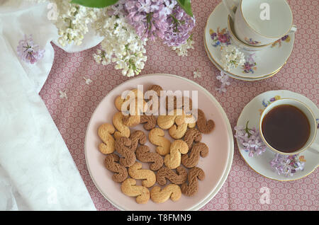 Tchèque traditionnel de la cannelle & cacao biscuits Esicka sur une plaque sur une table en bois avec un vieux-fashionned tasse de thé et de fleurs lilas. Banque D'Images