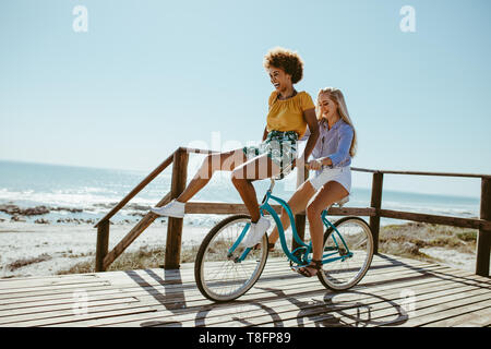 Woman riding a bicycle avec son ami assis sur le guidon. Deux filles sur le vélo ayant beaucoup de plaisir.