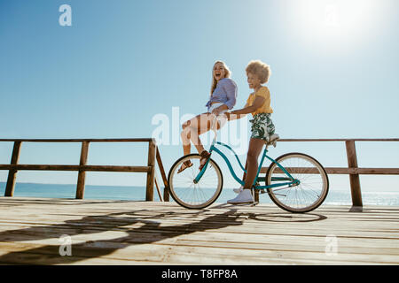 Jeune femme équitation un cycle avec son ami assis sur le guidon sur la promenade de bord de mer. Deux jeunes filles de profiter en vtt sur une journée d'été.