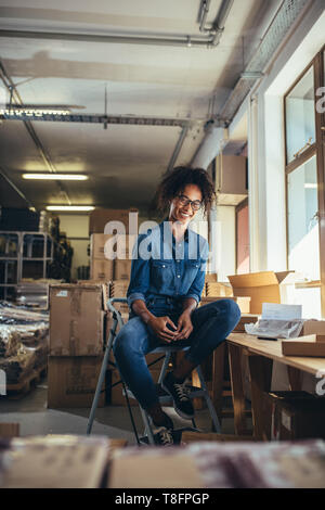 Propriétaire d'entreprise en ligne assise à son bureau. Jeune femme avec des boîtes d'expédition autour de looking at camera et souriant. Banque D'Images