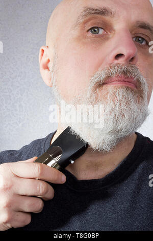 Homme aux cheveux gris se rase la barbe avec un rasoir électrique Banque D'Images