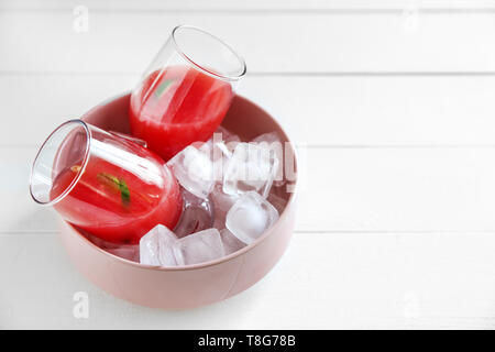 Lunettes avec fresh watermelon smoothie et de cubes de glace dans un bol sur la table en bois blanc Banque D'Images