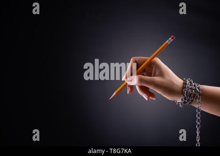 Femme la main avec un crayon jaune attaché avec chaîne, illustrant l'idée de la liberté de la presse ou la liberté d'expression sur fond sombre en bas-clé. Worl Banque D'Images