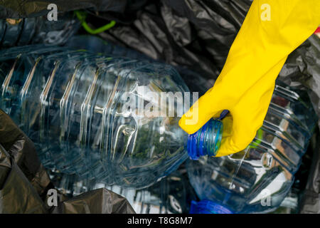 Séparer la collecte des déchets. La main dans le gant jaune grande mise en bouteilles en plastique sac poubelle en plastique bllack. Banque D'Images