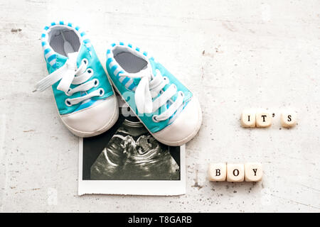 Chaussons pour bébé bleu avec une photo de l'échographie pendant 20 semaines sur un fond clair. C'est inscription boy Banque D'Images