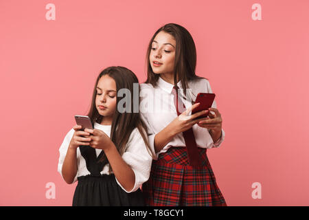 Portrait de jeunes filles en uniforme d'aide tandis que les smartphones isolés sur fond rouge Banque D'Images