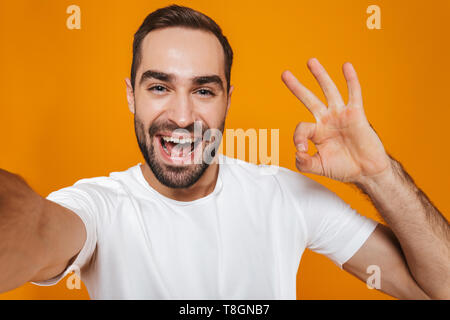 Portrait de unshaved man 30s en t-shirt en souriant tout en prenant des photos de selfies isolé sur fond jaune Banque D'Images