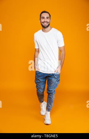 Longueur totale image guy 30s en t-shirt et jeans smiling while isolés sur fond jaune Banque D'Images