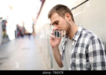 Vue latérale d'un triste portrait man talking on phone seul dans une rue solitaire Banque D'Images