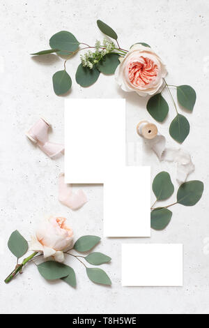 La papeterie de mariage, anniversaire maquette des lieux. Cartes de voeux vierges, de rubans de soie, des feuilles d'eucalyptus et blush pink roses anglaises fleurs. Le béton blanc Banque D'Images