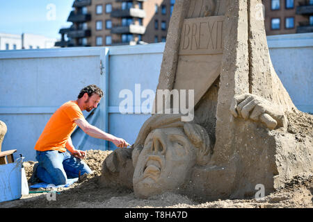 Artiste sculptures de sable Johannes Hogebrink travaille sur un Brexit sculpture à thème au Festival de sculptures de sable, Weston Weston-super-Mare, avec premier ministre Theresa peut réduire sa propre tête à l'aide d'une guillotine. Banque D'Images