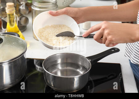 Woman pouring riz cru dans la casserole d'eau bouillante sur la cuisinière Banque D'Images