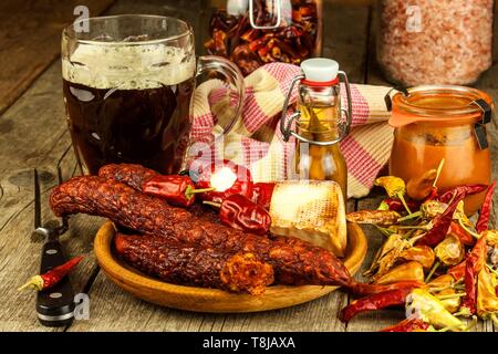 Bière brune dans un verre et saucisses épicées avec des piments. Saucisses séchées sur la table. Banque D'Images