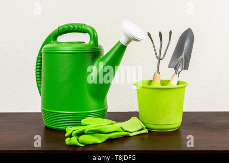 D'un coup horizontal Arrosoir vert avec du blanc bec avec une truelle et fourche de jardinage dans un pot vert vert avec des gants de jardinage à côté d'eux. Wo Banque D'Images