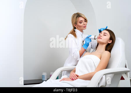 Jolie blonde doctor coiffeur rf-Procédure de levage pour femme fixant dans un salon de beauté. Cosmétologie matérielles. Patient recevant electric f Banque D'Images