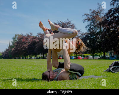 Les jeunes athletic couple in love performing yoga acro dans Roath Park par une belle journée ensoleillée. Banque D'Images