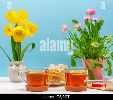 La vie toujours avec des tasses de thé, morceaux de gâteau, bouquet de fleurs roses dans un pot rose, guimauve et bougie en forme de coeur et fleurs tulipes jaune sur un Banque D'Images