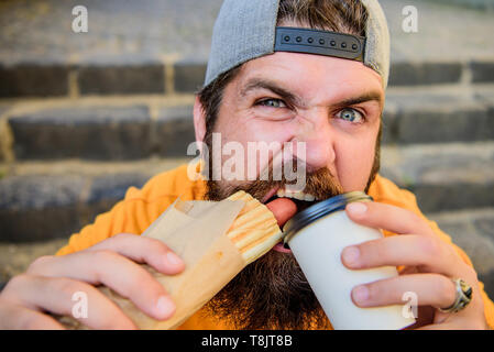 Se libérer de la faim et de la soif. Homme barbu ayant hot-dog et le café pour pause gourmande. Portrait guy profiter de la restauration rapide et de boisson chaude pour pause repas. Hipster snacking sur des escaliers pendant de repos. Banque D'Images