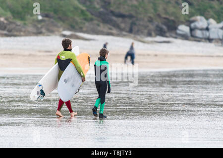 Un père et son fils avec leurs planches de surf et de marcher à travers la plage de Fistral, Newquay en à Cornwall. Banque D'Images