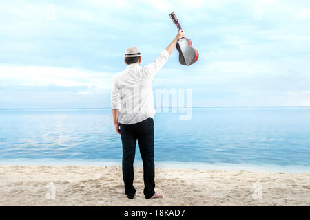 Vue arrière du businessman hat et white clothes holding la guitare sur la plage. Vacances d'été Banque D'Images