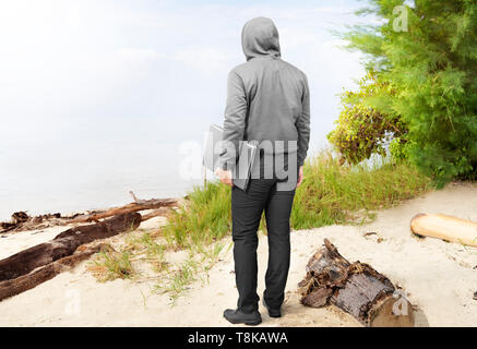 Vue arrière de l'homme en noir hoodie exerçant son portable dans sa main sur la plage Banque D'Images