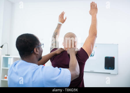 Sportsman élever les mains tout en ayant l'examen médical jusqu'au thérapeute Banque D'Images