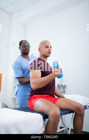 Thérapeute à peau sombre dans les verres en regardant son patient faisant des exercices Banque D'Images