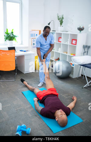Debout près de thérapeute patient avec blessure à la jambe allongée sur mat Banque D'Images