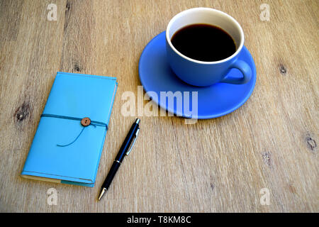 Café noir dans une grande tasse, stylo bleu et bleu notes sur une table en bois Banque D'Images