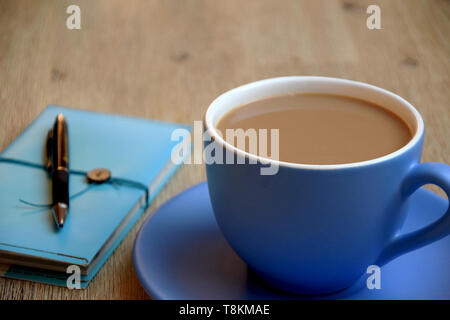 Café avec du lait dans une grande tasse, stylo bleu et bleu notes sur une table en bois Banque D'Images